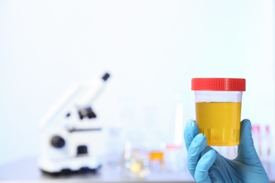Laboratory assistant holding urine sample in container indoors, closeup with space for text. Medical analysis
