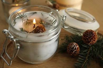 Photo of Burning scented conifer candle and Christmas decor on wooden table, closeup