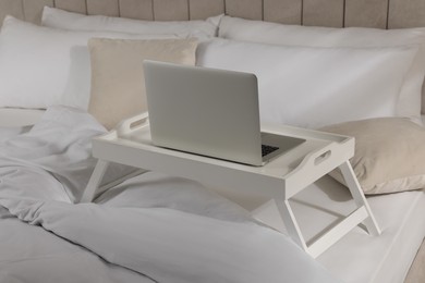 White tray table with laptop on bed