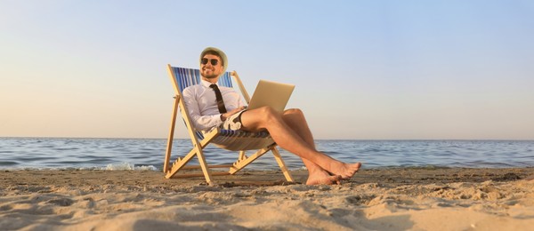 Photo of Happy man with laptop resting on deckchair near sea. Business trip