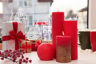 Photo of Beautiful burning candles with Christmas decor on white wooden table near window