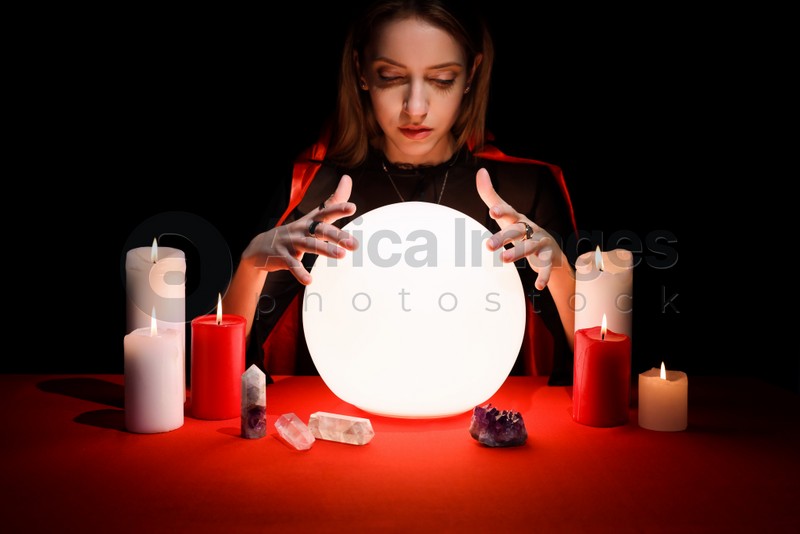 Soothsayer using glowing crystal ball to predict future at table in darkness. Fortune telling