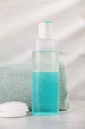 Bottle of micellar water, towel and cotton pads on white table against marble background