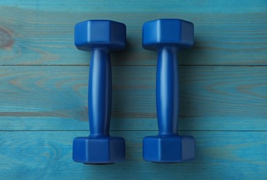 Blue dumbbells on turquoise wooden table, flat lay