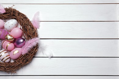 Photo of Festively decorated Easter eggs, vine wreath and feathers on white wooden table, top view. Space for text