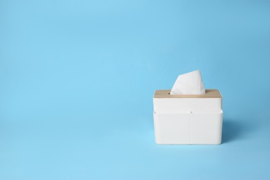 Holder with paper tissues on light blue background. Space for text