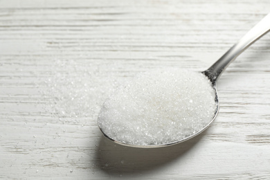 Photo of Spoon of sugar on white wooden table, closeup