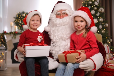 Santa Claus and little children with presents in room decorated for Christmas