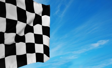 Checkered racing finish flag against blue sky. Space for text