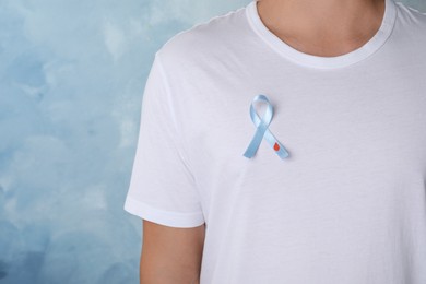Man with light blue ribbon and paper blood drop on color background, closeup. World Diabetes Day