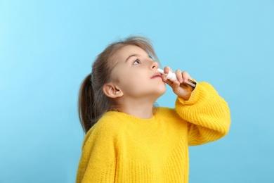 Sick little girl using nasal spray on light blue background