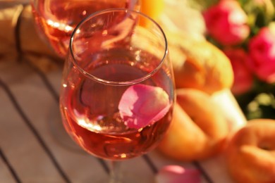 Photo of Glass of delicious rose wine with petals and peaches outside, closeup