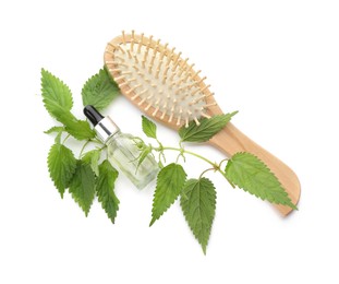 Photo of Stinging nettle extract in bottle, green leaves and brush on white background, top view. Natural hair care