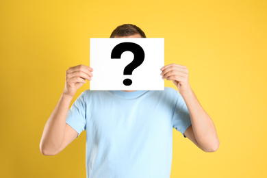 Man holding paper with question mark on yellow background