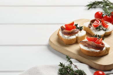 Photo of Delicious sandwiches with cream cheese, anchovies and tomatoes on white wooden table, space for text