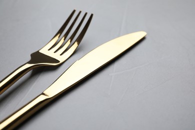 Golden fork and knife on light grey table, closeup. Space for text