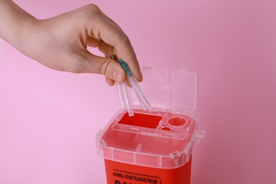 Woman throwing used syringe needles into sharps container  on pink background, closeup