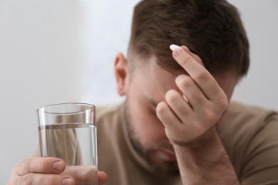 Man with glass of water and pill suffering from migraine, closeup