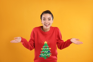 Surprised young woman in Christmas sweater on yellow background