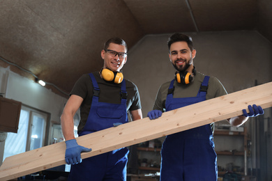 Professional carpenters with large wooden board in workshop	