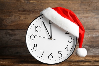 Clock with Santa hat showing five minutes until midnight on wooden background. New Year countdown