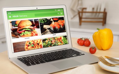 Modern laptop with open page for online food ordering on table in kitchen. Delivery service