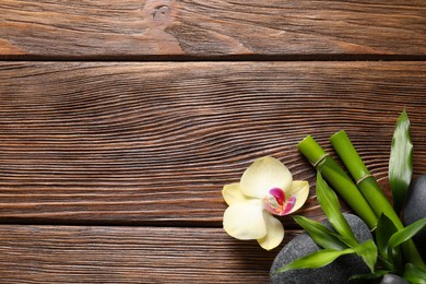 Spa stones, orchid flower and bamboo stems on wooden background, flat lay. Space for text