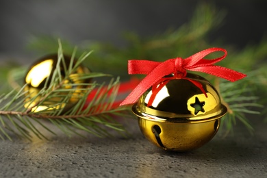 Golden sleigh bells and fir branches on grey background, closeup