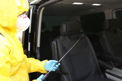 Person in protective suit disinfecting car with sprayer. Preventive measure during coronavirus pandemic