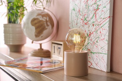 Modern night lamp and decor on table near pink wall. Space for text