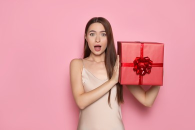 Photo of Portrait of emotional young woman with gift box on pink background
