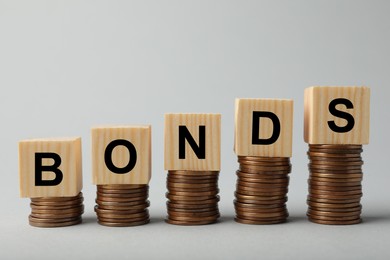 Photo of Word Bonds made of wooden cubes with letters on stacked coins against light grey background