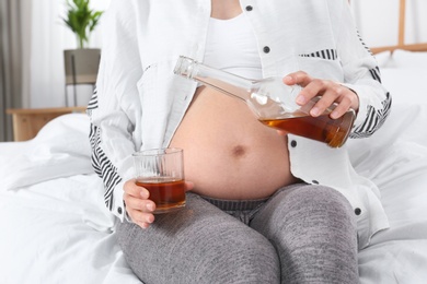 Pregnant woman pouring whiskey into glass at home. Alcohol addiction
