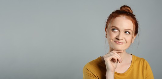 Portrait of thoughtful red haired woman with charming smile on grey background