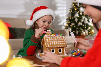 Mother and daughter decorating gingerbread house at table indoors