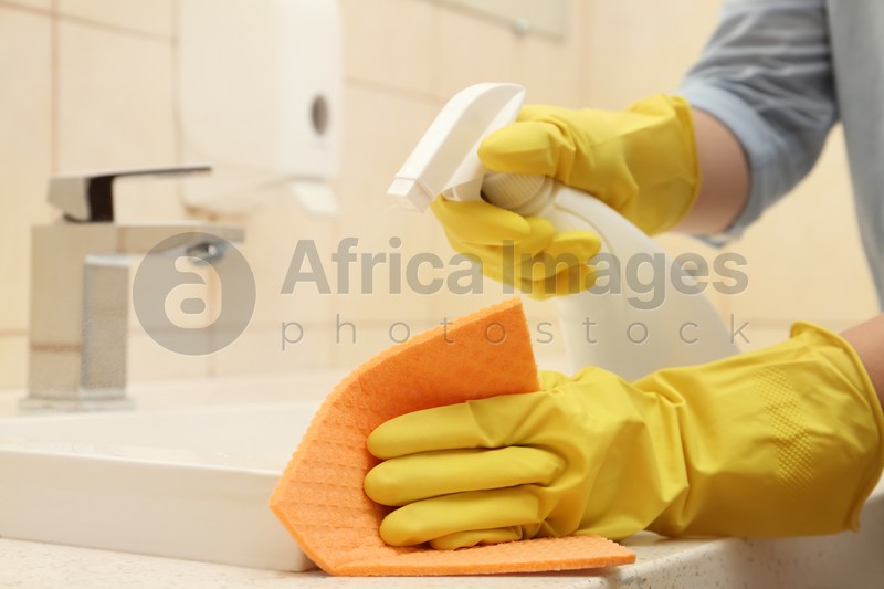Woman cleaning sink with detergent and rag in bathroom, closeup