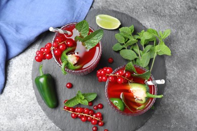 Glasses of spicy red currant cocktail with jalapeno and mint on grey table, flat lay