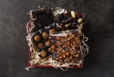 Box with chocolate and sweets on dark grey table, top view