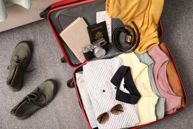 Photo of Open suitcase with clothes, accessories and shoes on floor, flat lay