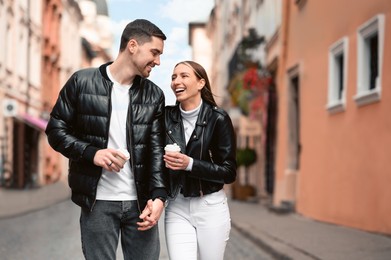 Photo of Lovely young couple with cups of coffee walking together on city street. Romantic date
