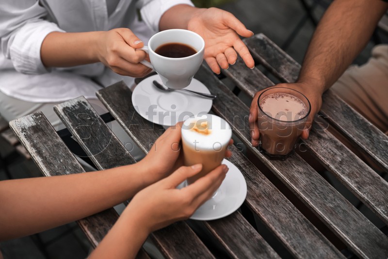 Friends drinking coffee and cocoa at wooden table in outdoor cafe, closeup