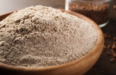 Bowl of buckwheat flour on wooden table, closeup