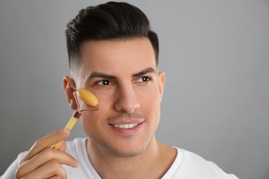 Man using mineral facial roller on grey background. Space for text