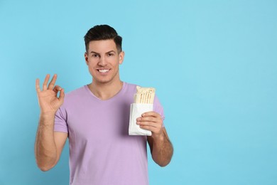 Man with delicious shawarma on turquoise background, space for text