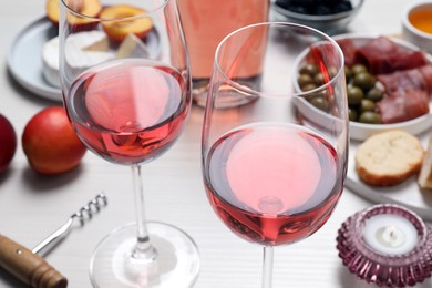 Photo of Glasses of delicious rose wine and snacks on white table, closeup