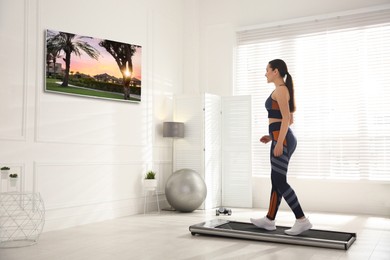 Sporty woman training on walking treadmill and watching TV at home