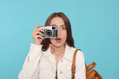 Photo of Emotional young woman with camera taking photo on light blue background. Interesting hobby
