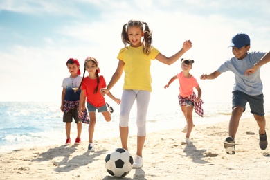 Photo of Cute children playing soccer at beach on sunny day. Summer camp