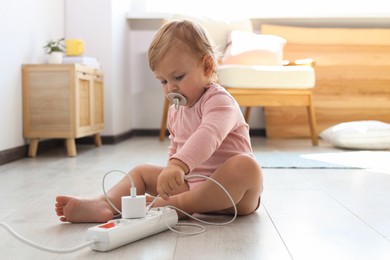 Photo of Cute baby playing with charger on floor at home. Dangerous situation