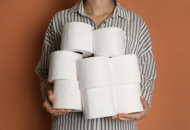 Woman with heap of toilet paper rolls on brown background, closeup